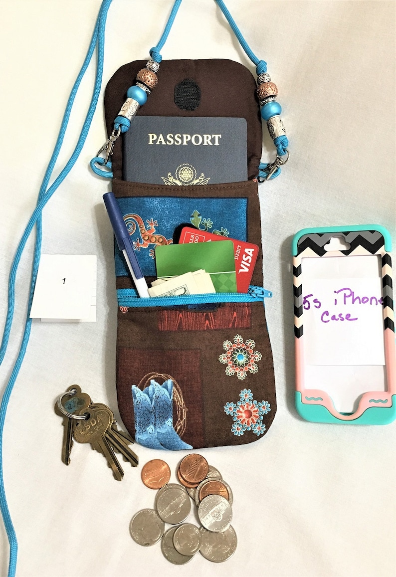 May include: A brown fabric pouch with a zipper closure and a blue and white patterned design. The pouch is hanging from a blue lanyard with silver and brown beads. The pouch is open and contains a passport, credit cards, cash, a pen, and keys. A cell phone case with the text "5s iPhone Case" is also visible.