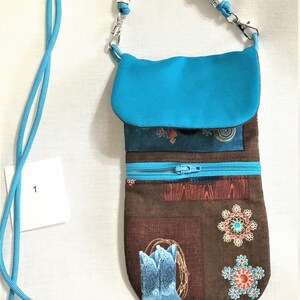 May include: A turquoise blue fabric pouch with a zipper closure and a brown fabric base with a western-themed print featuring boots, flowers, and geometric patterns. The pouch has a long turquoise blue strap with silver beads.