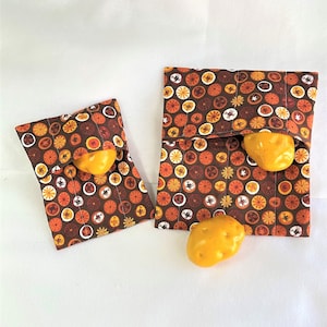 May include: Two brown fabric pouches with a repeating pattern of orange and white circles on a brown background. The pouches are filled with yellow potatoes.