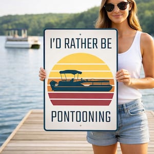 May include: A rectangular sign with the text "I'D RATHER BE PONTOONING" above a graphic of a pontoon boat and a sunset. The sign is held by a person on a wooden dock, with a lake and trees in the background.