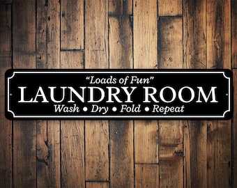May include: Black and white sign with the text "Loads of Fun" Laundry Room Wash, Dry, Fold, Repeat on a wood background.