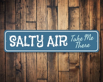 May include: A blue metal sign with white text that reads "Salty Air Take Me There". The sign has a distressed look and is perfect for a beach house or nautical themed decor.