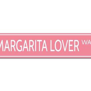 May include: Pink metal sign with white text that reads "Margarita Lover Way".