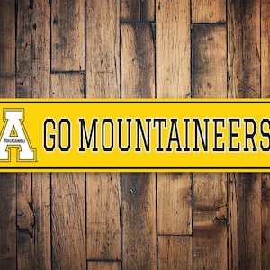 May include: Yellow and black metal sign with the letter "A" and the words "Go Mountaineers!"