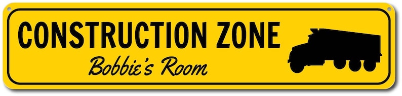 May include: Yellow construction zone sign with black text that reads "CONSTRUCTION ZONE" and "Bobbie's Room" with a black silhouette of a dump truck on the right side.