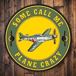 May include: A green and yellow round metal sign with the text "Some Call Me Plane Crazy" and a cartoon image of a green and brown airplane.
