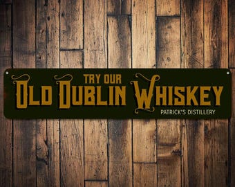 Puede incluir: Un letrero de metal verde oscuro con letras doradas que dice "Try Our Old Dublin Whiskey Patrick's Distillery".