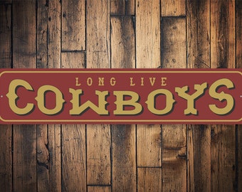 Może przedstawiać: Metalowy znak w kolorze czerwonym z pozłacanymi literami, na którym widnieje napis "Long Live Cowboys".