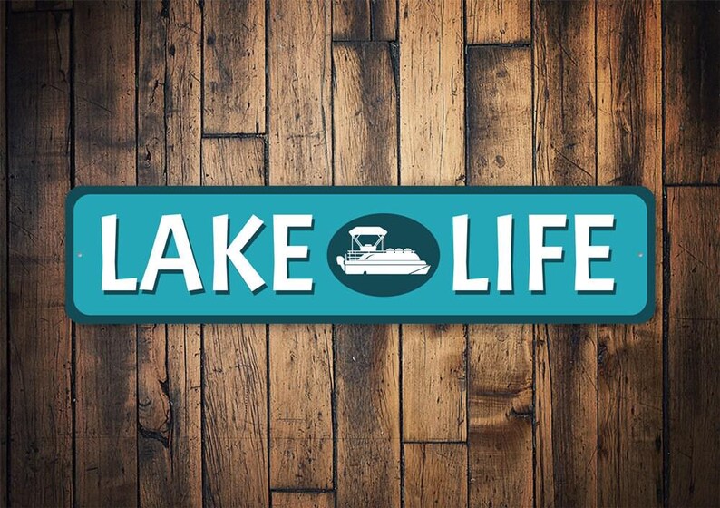 May include: A teal blue metal sign with white text that reads "LAKE LIFE". A white silhouette of a pontoon boat is in a circle in the middle of the sign.