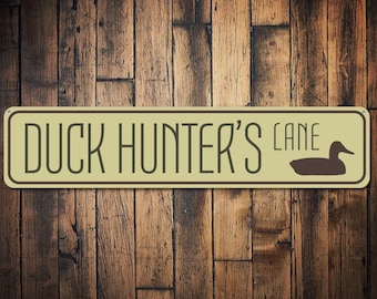 Op de afbeelding: Een rechthoekig bord in tan en bruin met de tekst "Duck Hunter's Lane" en een silhouet van een eend in de vlucht.