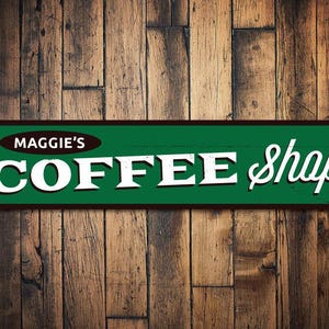 May include: A green and brown metal sign with white lettering that reads "Maggie's Coffee Shop".