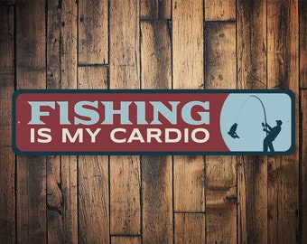以下が含まれることがあります： 「Fishing is my cardio」という文字と、釣りをしている人のシルエットが描かれた赤と青の金属製の看板です。