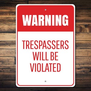 May include: A rectangular red and white warning sign with the text "WARNING" at the top and "TRESPASSERS WILL BE VIOLATED" below. The sign is set against a wooden background.