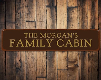 May include: A brown metal sign with gold lettering that reads "The Morgan's Family Cabin".