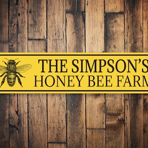 May include: A yellow sign with black text and a black and white bee illustration. The sign reads "The Simpson's Honey Bee Farm".