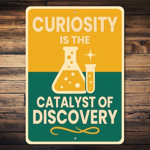 May include: A rectangular sign with a yellow and green background. The sign features the text "CURIOSITY IS THE CATALYST OF DISCOVERY" in white, along with illustrations of laboratory beakers. The sign is mounted on a wooden surface.