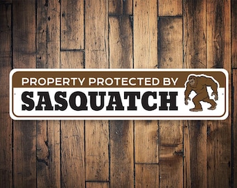 Op de afbeelding: Een wit bord met bruine letters met de tekst "Property Protected by Sasquatch". Aan de rechterkant van het bord is een cartoon Sasquatch afgebeeld.