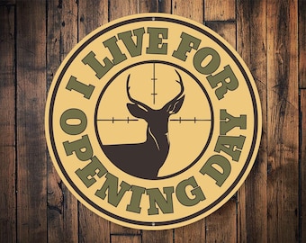 May include: A yellow and green round sign with the text "I Live For Opening Day" and a silhouette of a deer in a crosshair.