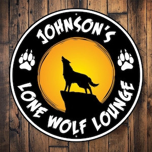 May include: A black and white circular sign with the text "Johnson's Lone Wolf Lounge" in a white circle with a yellow sun and a black silhouette of a wolf howling at the moon. The sign has two paw prints on either side of the circle.