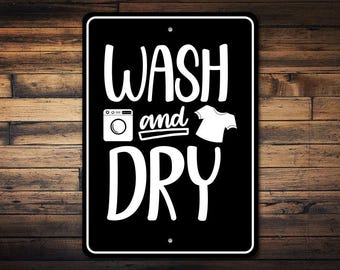 May include: Black and white sign with the text "WASH and DRY" in a stylized font. The sign also includes an illustration of a washing machine and a t-shirt.