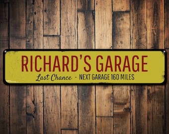 Puede incluir: Un letrero de metal amarillo con borde negro y esquinas redondeadas. El letrero dice "Richard's Garage" en letras rojas con el texto "Last Chance - Next Garage 160 Miles" en letras rojas más pequeñas.