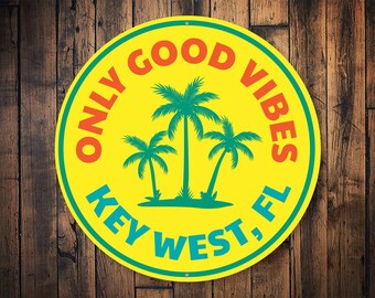 May include: A yellow round sign with a teal border and the text "ONLY GOOD VIBES KEY WEST, FL" in a white, teal, and orange font. Three green palm trees are in the center of the sign.