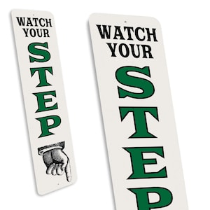 two identical signs with the text "WATCH YOUR STEP" in green and black lettering.