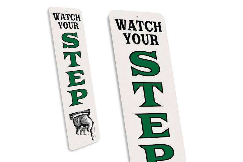 two identical signs with the text "WATCH YOUR STEP" in green and black lettering.