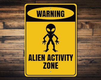 May include: A yellow warning sign with black text and a black alien silhouette. The sign reads "Warning Alien Activity Zone".