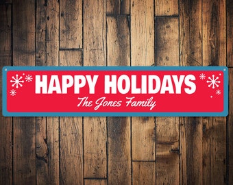 May include: A red and blue metal sign with white text that reads "HAPPY HOLIDAYS" and "The Jones Family". The sign has snowflake designs on the left and right sides.