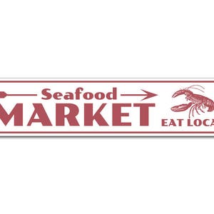 Op de afbeelding: Een wit rechthoekig bord met rode tekst en een pijl die naar rechts wijst. De tekst luidt "Seafood Market" en "Eat Local". Aan de rechterkant van het bord staat een rode kreeft-illustratie.