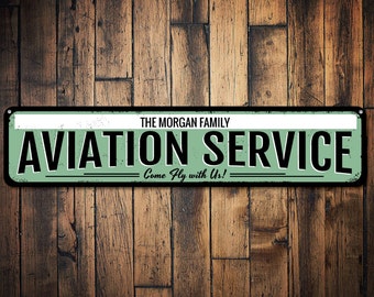 Peut inclure: Une enseigne en métal de style vintage avec un fond vert et des lettres noires. L'enseigne indique "The Morgan Family Aviation Service - Come Fly with Us!"