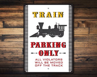 Può includere: Un cartello bianco con binari ferroviari neri sui lati. Il cartello dice "Train Parking Only" in lettere rosse con un'illustrazione di treno nero sopra il testo. Il cartello dice anche "All violators will be moved off the track" in lettere nere.