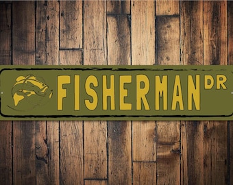 以下が含まれることがあります： 「FISHERMAN DR」という文字と魚のシルエットが描かれた緑と黄色の金属製の看板。自宅やお店に最適です。
