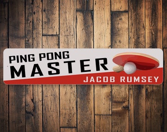 May include: A white and red sign with the text "PING PONG MASTER" and the name "JACOB RUMSEY". A red and white ping pong paddle and ball are shown on the right side of the sign.
