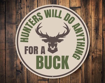 May include: A round, beige sign with a brown border and green text that reads "Hunters Will Do Anything For A Buck". A brown silhouette of a deer head is in the center of the sign.