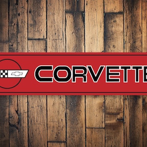 May include: Red metal sign with a black Corvette logo and the word "CORVETTE" in black letters.