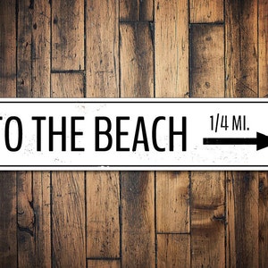May include: White sign with black text and arrow pointing right. The sign reads "To the Beach 1/4 Mi."