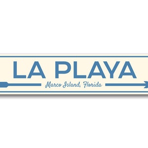 May include: A blue and white sign with the text "LA PLAYA Marco Island, Florida" and two arrows pointing in opposite directions.