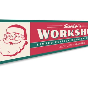 May include: A red and green metal sign with the text "Santa's Workshop" in white lettering. The sign also includes the text "Limited Edition Handcrafted Toys" and "Made Only for the North Pole". A cartoon image of Santa Claus is on the left side of the sign.