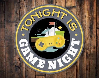Peut inclure: Une pancarte ronde, grise et jaune avec le texte "Tonight is Game Night" en blanc. La pancarte représente une manette de jeu vidéo de dessin animé avec une cartouche de jeu verte et jaune.