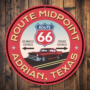 Puede incluir: Un letrero rojo y amarillo de punto medio de la Ruta 66 con un coche clásico rojo conduciendo por una carretera. El letrero dice "Route Midpoint Adrian, Texas" y "Route 66" con las distancias a Los Ángeles y Chicago.