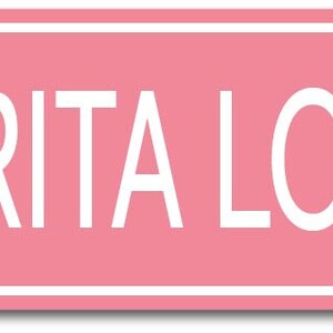May include: Pink rectangular sign with white border and white text that reads "MARGARITA LOVER WAY".