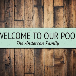 May include: A teal blue rectangular sign with black text that reads "Welcome to our pool The Anderson Family".