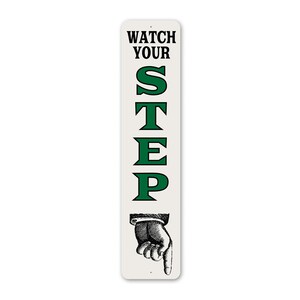 A sign with the text "WATCH YOUR STEP" in green letters, accompanied by a hand pointing downwards.