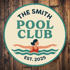 May include: Circular sign featuring "THE SMITH POOL CLUB" in teal and white, with a swimmer in a red swimsuit. The sign is cream-coloured with a teal border and the text "EST. 2025". Set against a wooden background.