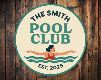 Puede incluir: Letrero redondo con el texto "THE SMITH POOL CLUB" en verde azulado y blanco. En el centro, una nadadora con traje de baño rojo. El letrero es de color crema con borde verde azulado y el texto "EST. 2025". Fondo de madera.
