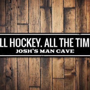 May include: Black and white sign with the text "ALL HOCKEY. ALL THE TIME. JOSH'S MAN CAVE" on a wood background.