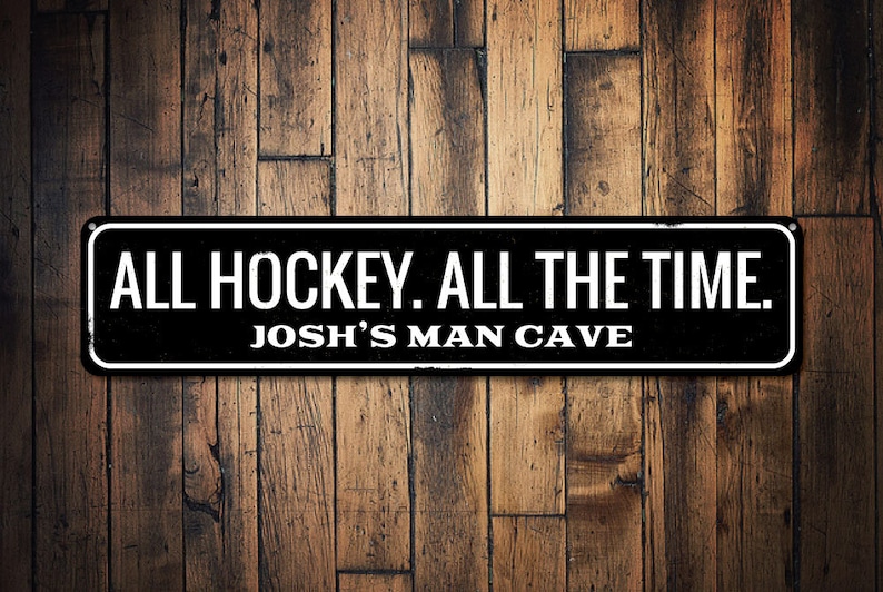 May include: Black and white sign with the text "ALL HOCKEY. ALL THE TIME. JOSH'S MAN CAVE" on a wood background.