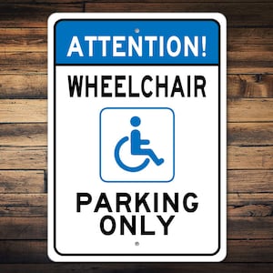 May include: White sign with blue text and a blue wheelchair symbol. The sign reads "ATTENTION! WHEELCHAIR PARKING ONLY".